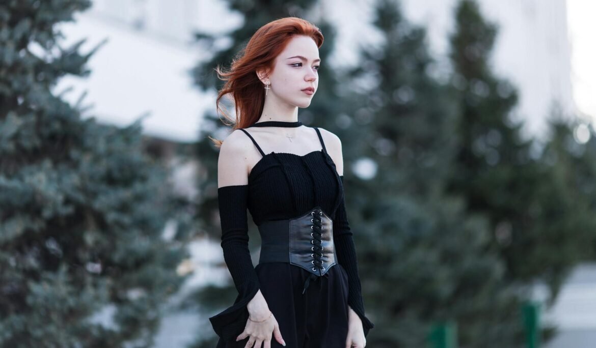 redhead woman in black outfit standing among evergreen trees